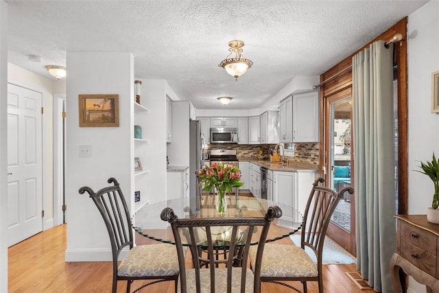 dining space with sink, a textured ceiling, and light wood-type flooring