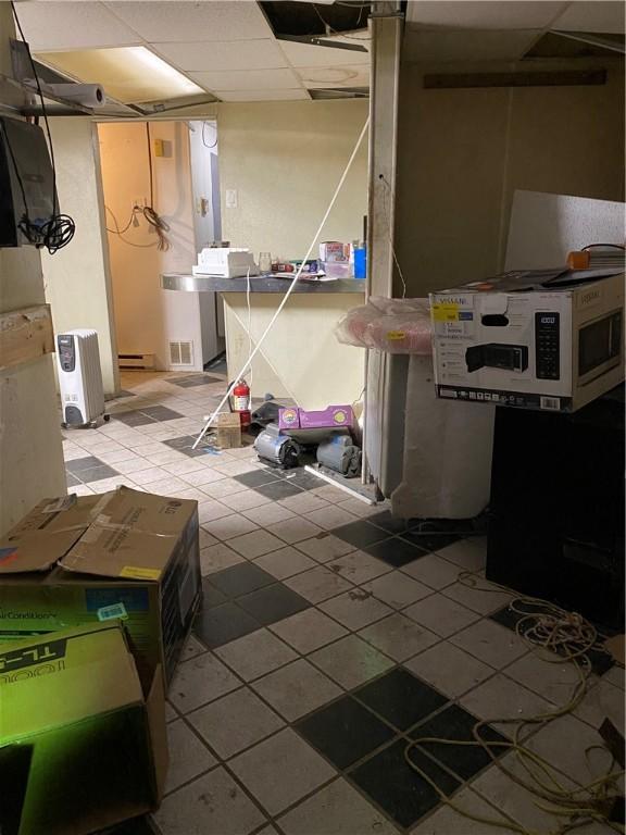 basement with light tile patterned flooring, a baseboard heating unit, and a paneled ceiling