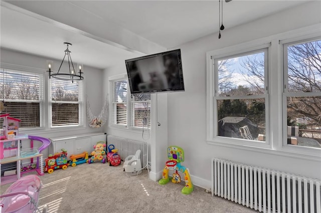 rec room with a wealth of natural light, radiator heating unit, a chandelier, and carpet