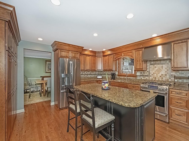 kitchen featuring appliances with stainless steel finishes, a breakfast bar, a center island, light stone counters, and wall chimney exhaust hood