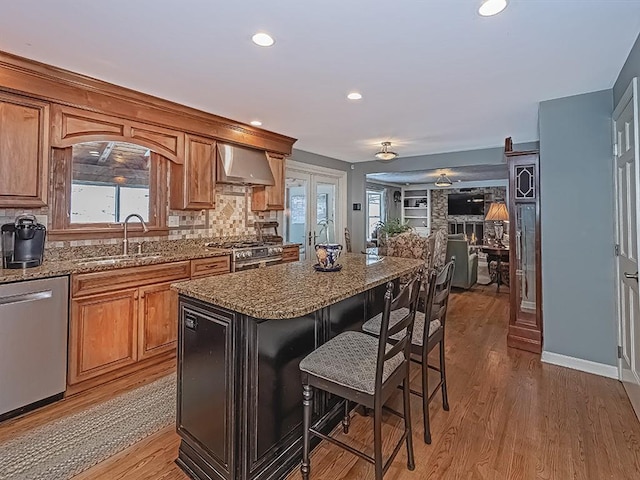 kitchen featuring a kitchen island, appliances with stainless steel finishes, sink, a breakfast bar area, and wall chimney range hood