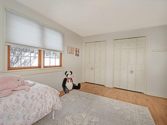 bedroom featuring light wood-type flooring, a textured ceiling, and two closets