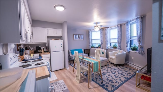 kitchen with white appliances, ceiling fan, a baseboard heating unit, white cabinets, and light wood-type flooring