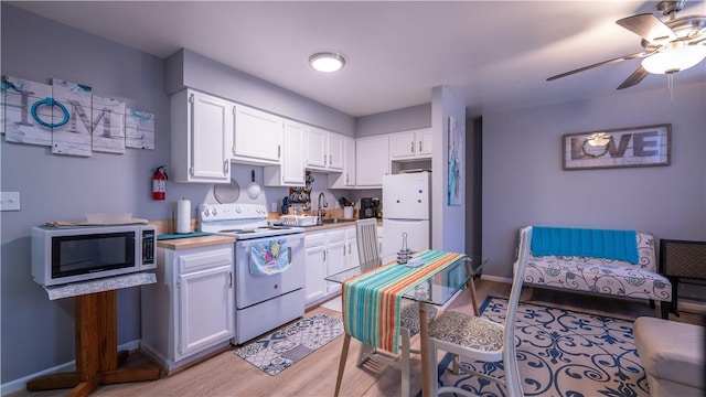 kitchen with light wood-style flooring, a ceiling fan, white cabinets, a sink, and white appliances