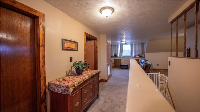 hall with carpet floors, baseboards, a textured ceiling, and an upstairs landing