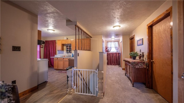 corridor with washer / dryer, baseboards, a textured ceiling, and an upstairs landing