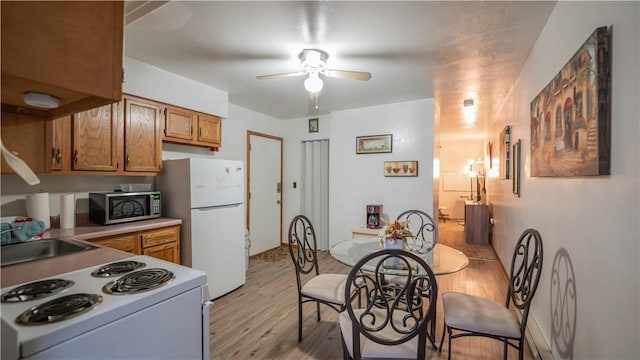 kitchen featuring brown cabinets, light wood finished floors, light countertops, ceiling fan, and white appliances