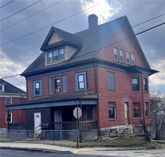 view of front facade with a fenced front yard, covered porch, brick siding, and a chimney