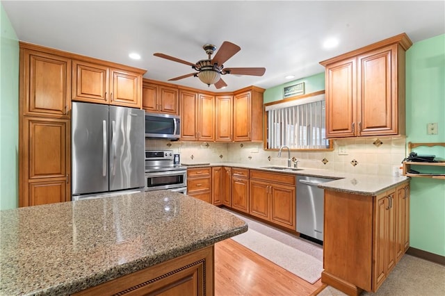 kitchen featuring sink, light stone counters, stainless steel appliances, light hardwood / wood-style floors, and backsplash