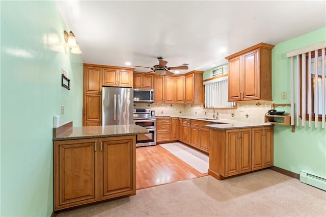 kitchen with sink, baseboard heating, stainless steel appliances, kitchen peninsula, and dark stone counters