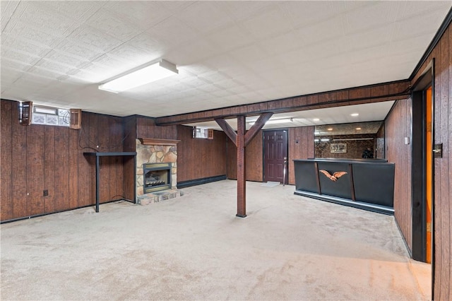 basement with a stone fireplace, light colored carpet, and wood walls