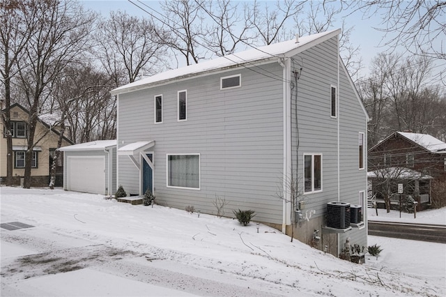 snow covered rear of property featuring a garage, central AC, and an outbuilding