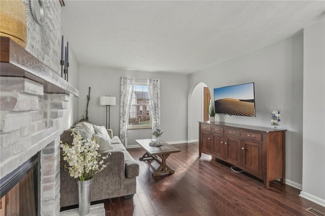 living room with a brick fireplace, dark hardwood / wood-style floors, and a textured ceiling