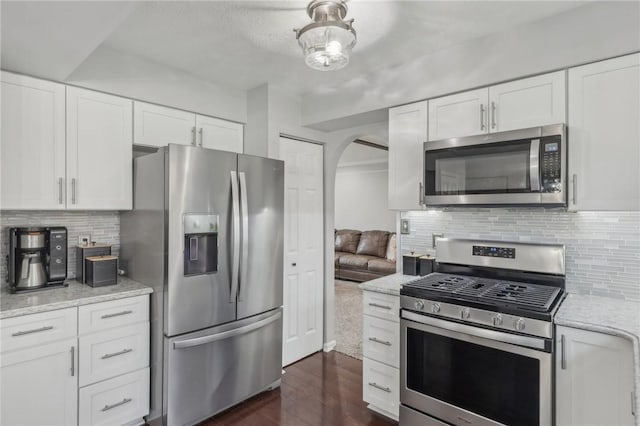 kitchen with light stone counters, appliances with stainless steel finishes, decorative backsplash, and white cabinets