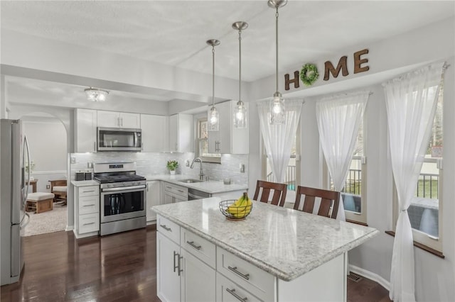 kitchen featuring sink, stainless steel appliances, light stone countertops, white cabinets, and decorative light fixtures