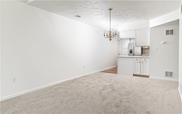 unfurnished living room with a chandelier, a textured ceiling, and dark colored carpet