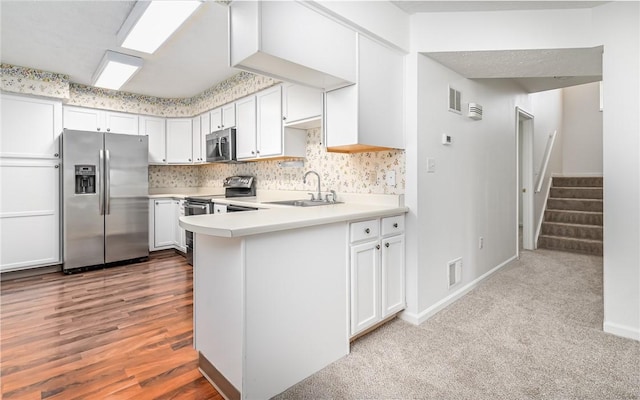 kitchen with sink, light hardwood / wood-style flooring, appliances with stainless steel finishes, white cabinetry, and decorative backsplash