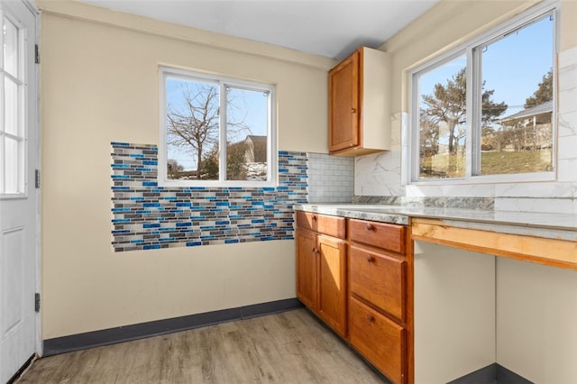 kitchen with light wood-type flooring, backsplash, brown cabinetry, and light countertops