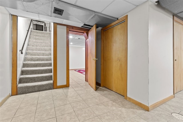 finished basement featuring visible vents, baseboards, stairway, light tile patterned floors, and a paneled ceiling