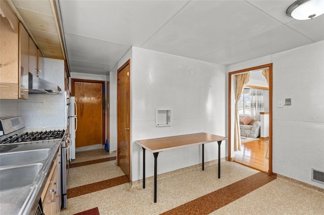 kitchen featuring visible vents, stainless steel range with gas cooktop, under cabinet range hood, freestanding refrigerator, and a sink