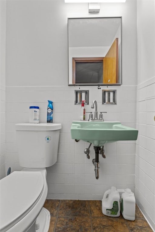 half bathroom featuring tile walls, toilet, and a wainscoted wall