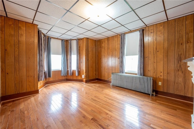 unfurnished room with radiator, wooden walls, light hardwood / wood-style floors, and a paneled ceiling