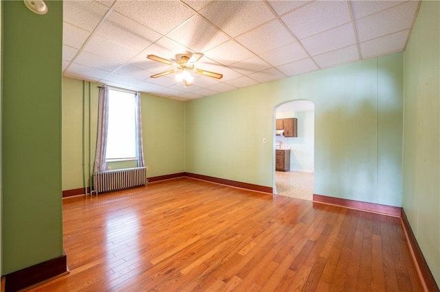 empty room with ceiling fan, a paneled ceiling, radiator, and hardwood / wood-style floors