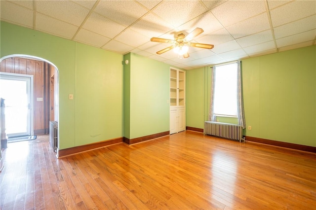 spare room with ceiling fan, a paneled ceiling, radiator heating unit, and light wood-type flooring