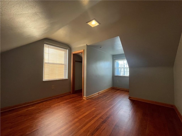 additional living space with hardwood / wood-style flooring, vaulted ceiling, and a textured ceiling