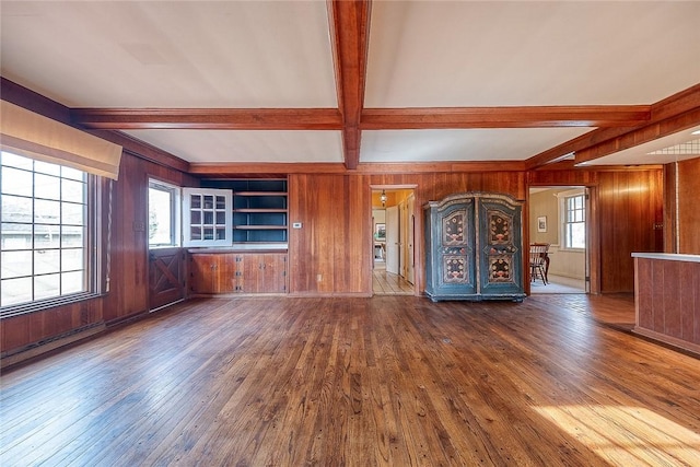 unfurnished living room featuring wood-type flooring, wooden walls, and beamed ceiling