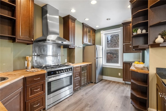 kitchen featuring wooden counters, dark brown cabinets, stainless steel appliances, light hardwood / wood-style floors, and wall chimney range hood