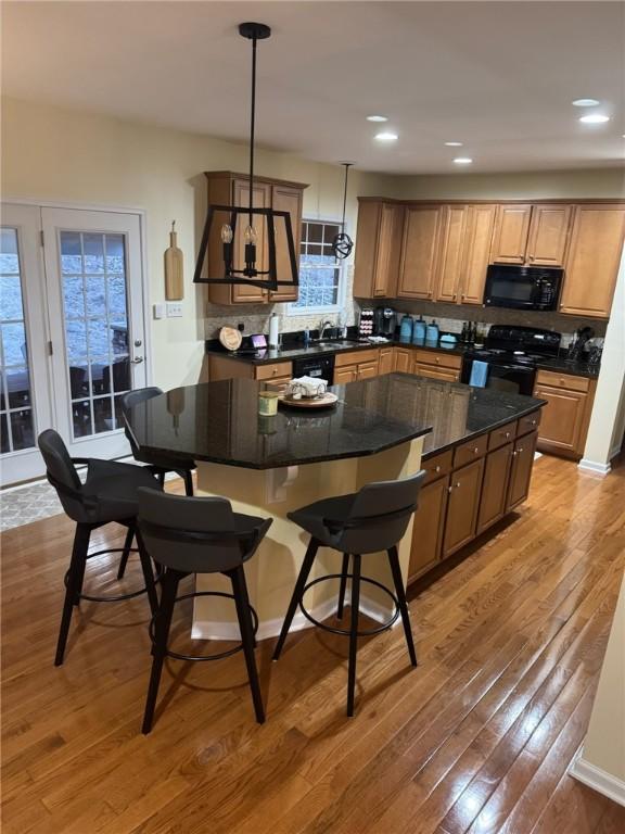 kitchen with black appliances, dark countertops, a kitchen island, and light wood-style flooring