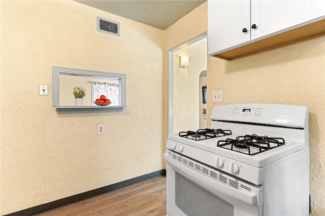 kitchen featuring white gas stove, white cabinets, and light hardwood / wood-style flooring