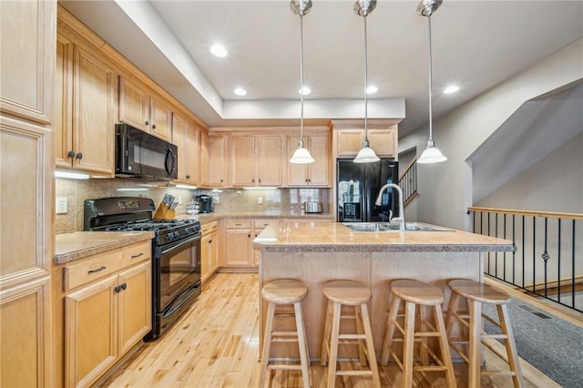 kitchen with a center island with sink, hanging light fixtures, a breakfast bar area, black appliances, and decorative backsplash