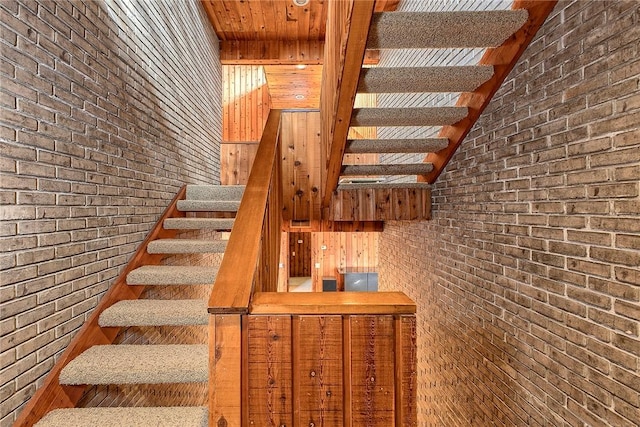 staircase featuring brick wall and vaulted ceiling with beams