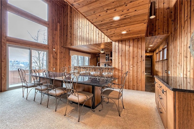 carpeted dining area featuring wooden ceiling, a high ceiling, and wood walls