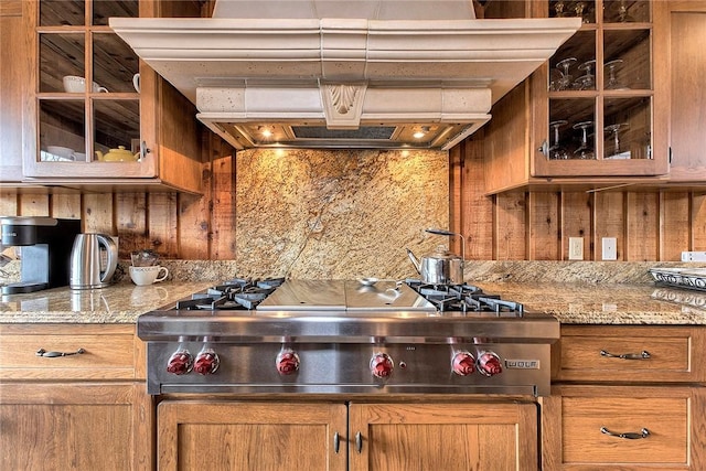 kitchen with extractor fan, stainless steel gas cooktop, wooden walls, and light stone counters