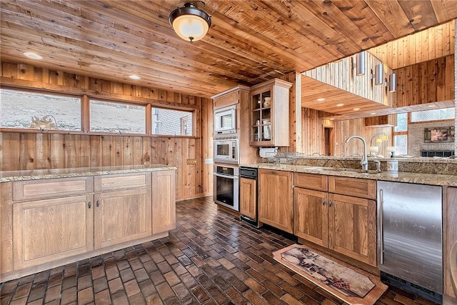 kitchen featuring wood walls, sink, wood ceiling, stainless steel appliances, and light stone countertops