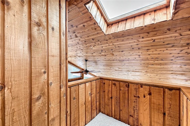 interior space with ceiling fan, a skylight, and wood walls