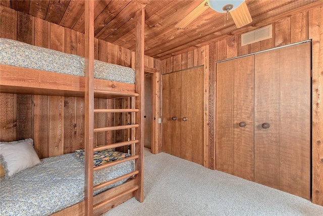 carpeted bedroom with multiple closets, wood ceiling, and wood walls