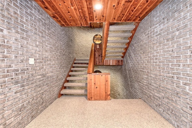 stairway featuring brick wall, wooden ceiling, and carpet