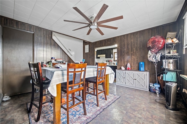 dining area with ceiling fan and wood walls