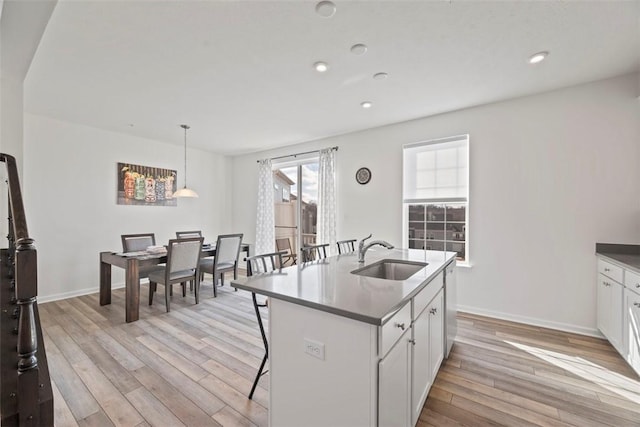 kitchen with sink, light hardwood / wood-style flooring, hanging light fixtures, an island with sink, and white cabinets