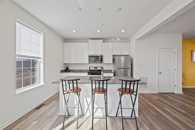 kitchen featuring a breakfast bar, appliances with stainless steel finishes, a kitchen island with sink, light hardwood / wood-style floors, and white cabinets