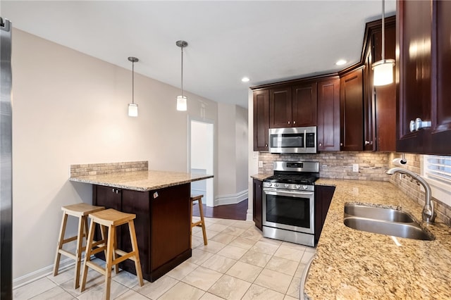 kitchen featuring a breakfast bar, sink, light stone counters, decorative light fixtures, and appliances with stainless steel finishes