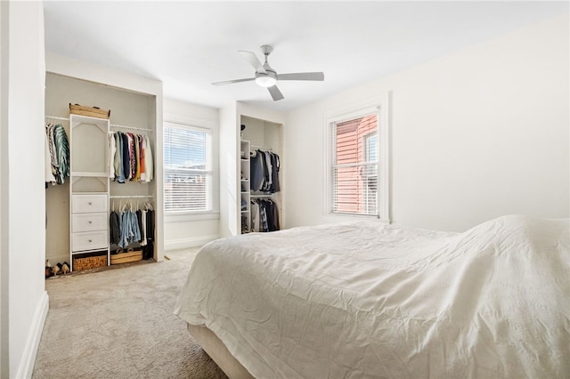 bedroom featuring two closets, light colored carpet, and ceiling fan