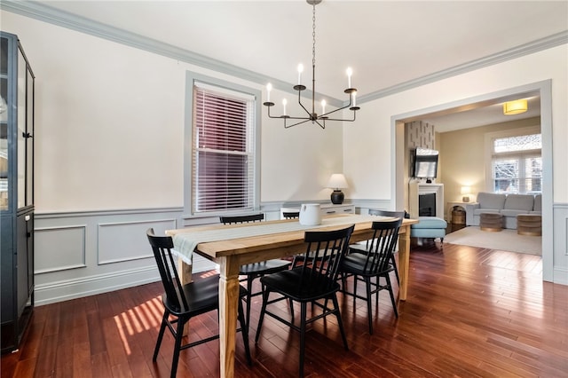 dining area featuring dark wood-type flooring, ornamental molding, and a notable chandelier