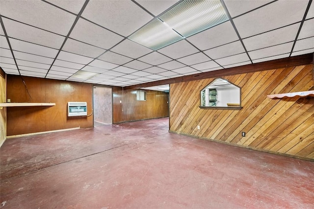 basement with heating unit, a drop ceiling, and wood walls