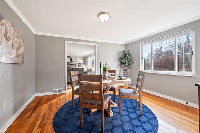 dining room featuring visible vents, crown molding, baseboards, and wood finished floors