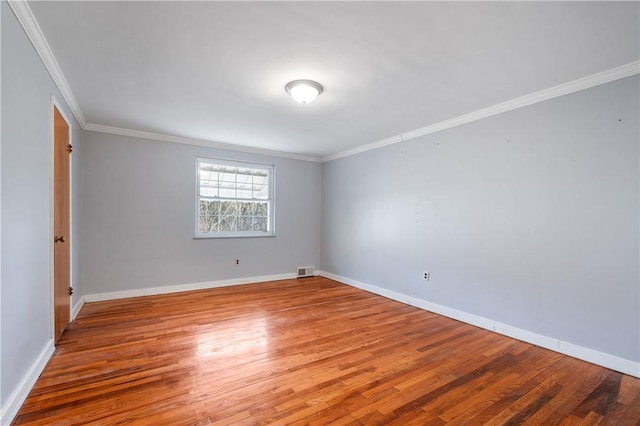 empty room featuring visible vents, crown molding, baseboards, and wood finished floors